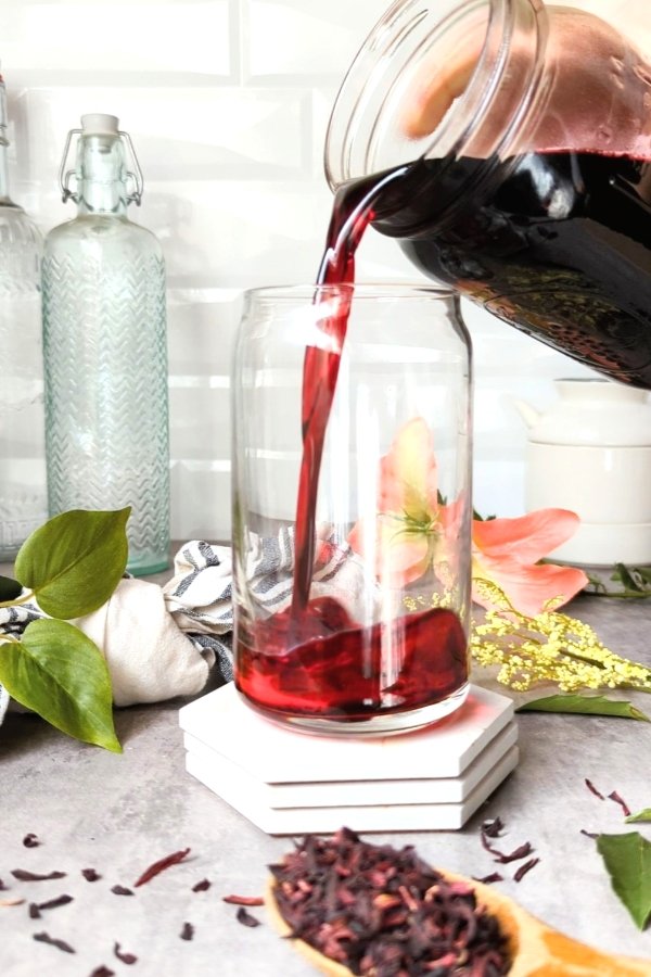 simple syrup with hibiscus flower tea recipe healthy hibiscus concentrate with dried flowers being poured into a glass.