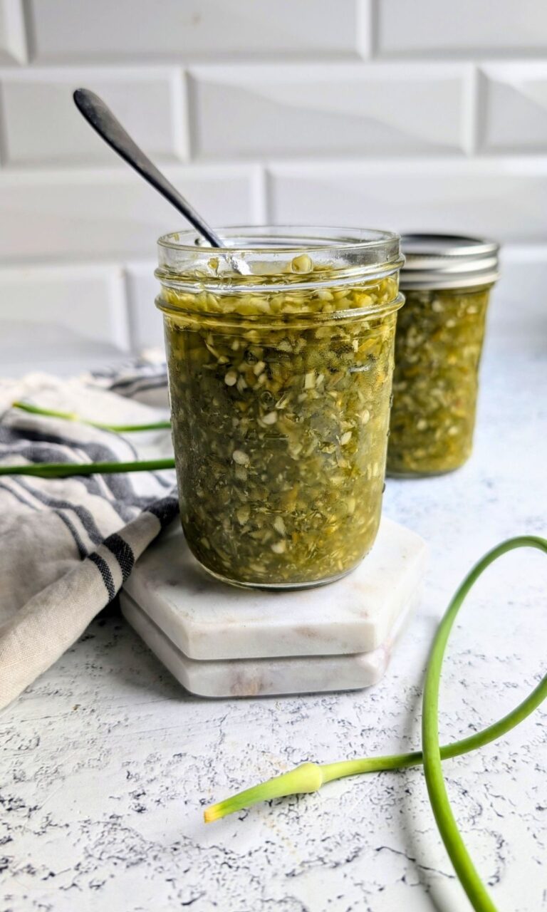 garlic scape hot sauce recipe with fresh scapes and jalapeno peppers in a jar with a spoon.